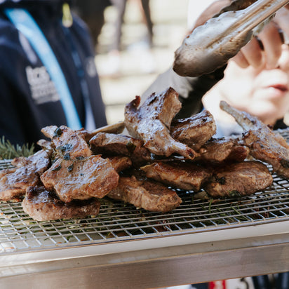 Grilled meat being turned on a barbecue grill with a person in the background.