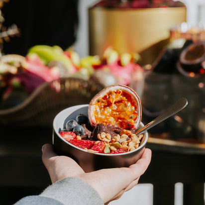 Hand holding a bowl of fruit acai bowl with a blurred background of a buffet table. Acai Bra. Acai Cart, Acai Toppings.