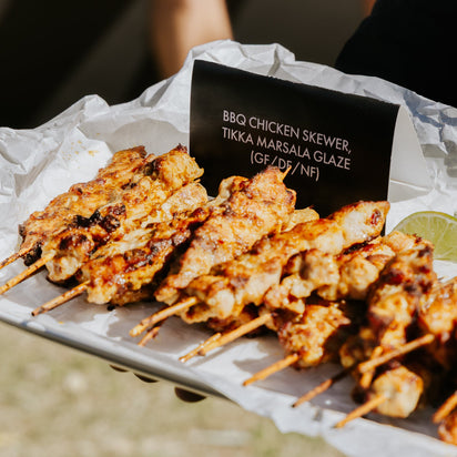 BBQ chicken skewers with Tikka Masala glaze on a white paper tray, accompanied by lime wedges.