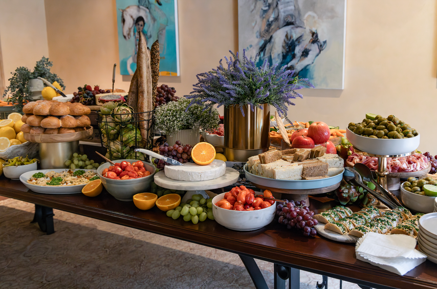 Table with a variety of food items including fruits, vegetables, and bread in a room with decorative elements. Large Grazing Table.