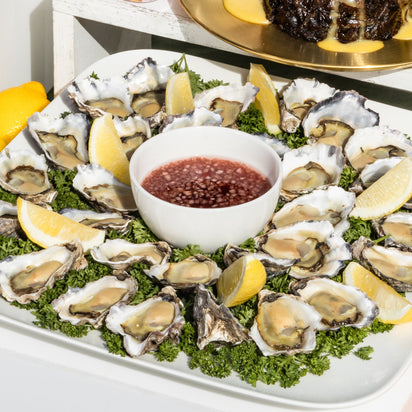 Platter of raw oysters on a bed of lettuce with lemon wedges and a small bowl of sauce.