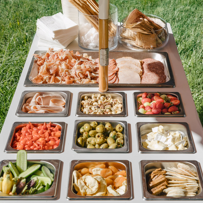 Outdoor setting with a platter of assorted snacks and a baseball bat on a grassy background. Grazing Cart.