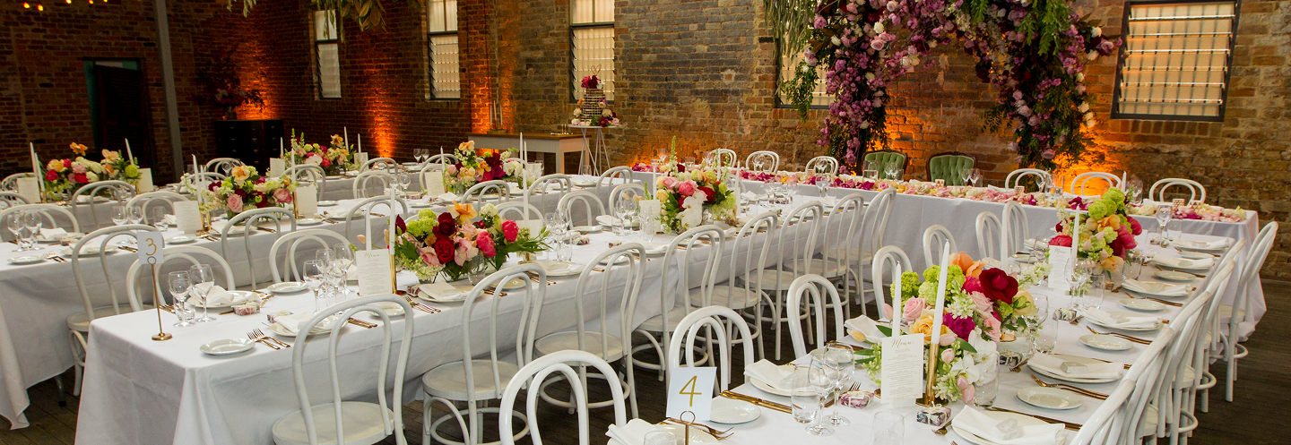 Wedding venue, long tables with brick walls, large florals, tables set up for dining.