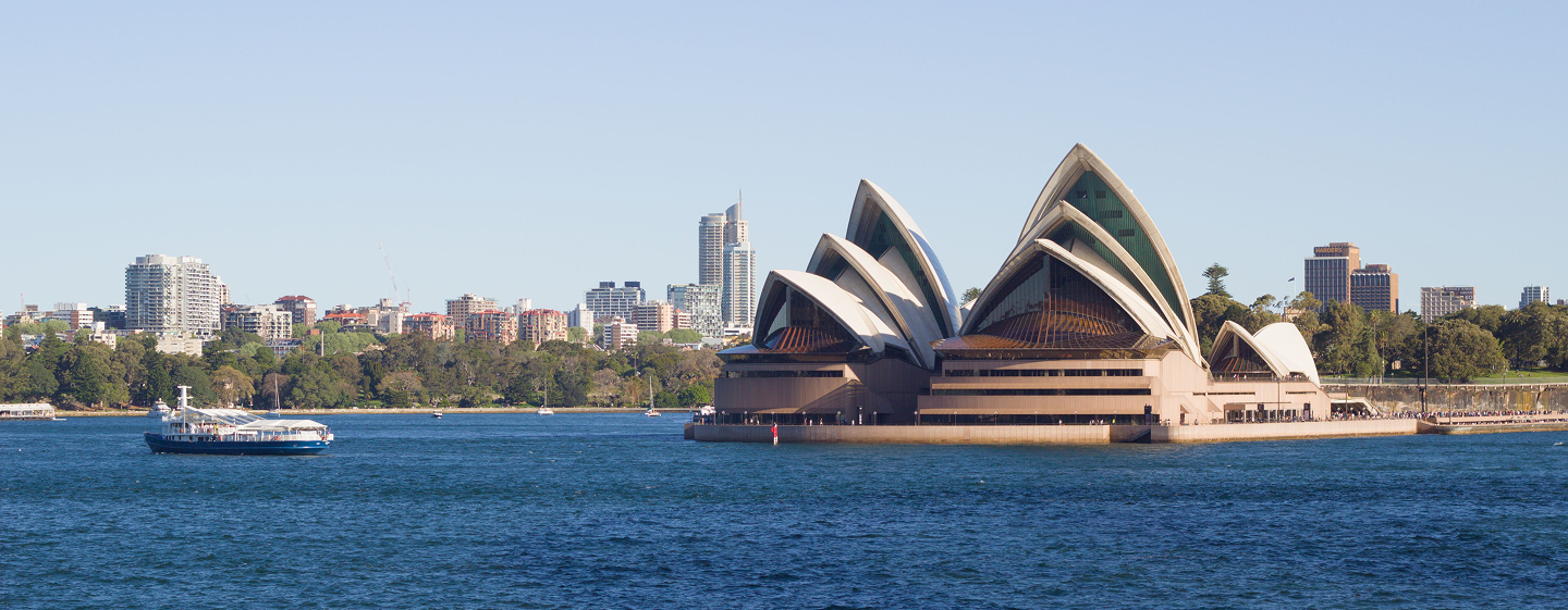 Sydney Opera House overlooking the harbor with the Sydney skyline and a ferry in the background under a clear blue sky.